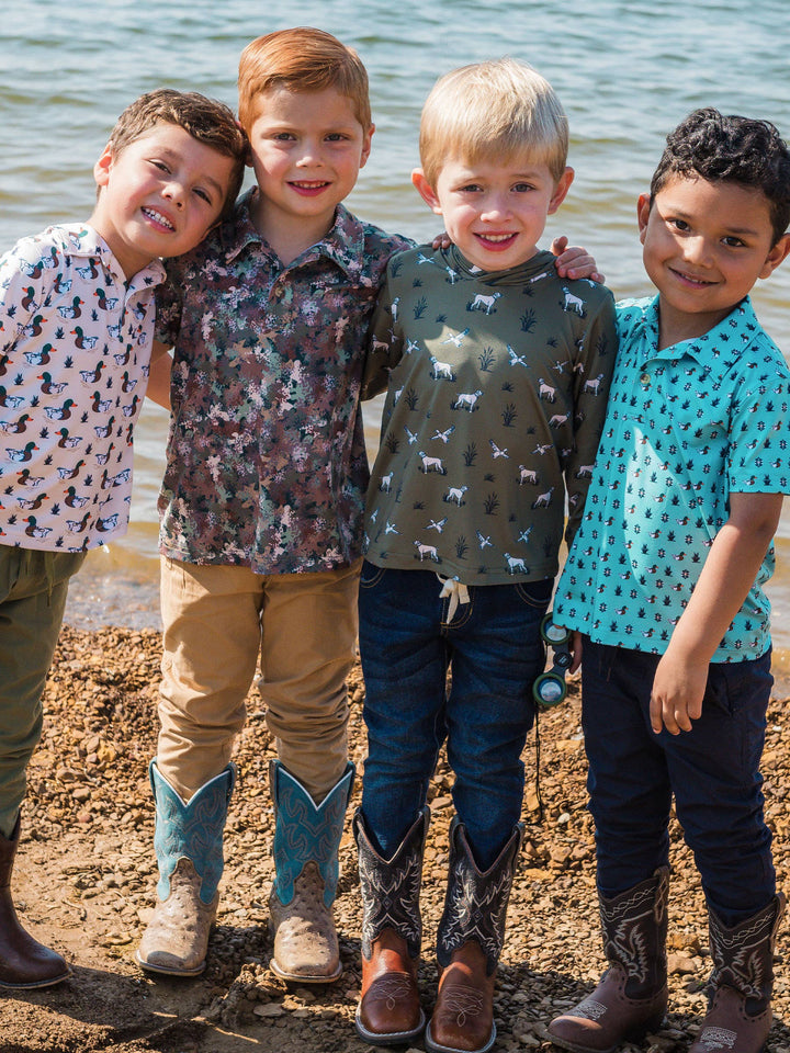 Four children standing together on a beach, wearing patterned shirts and boots.
